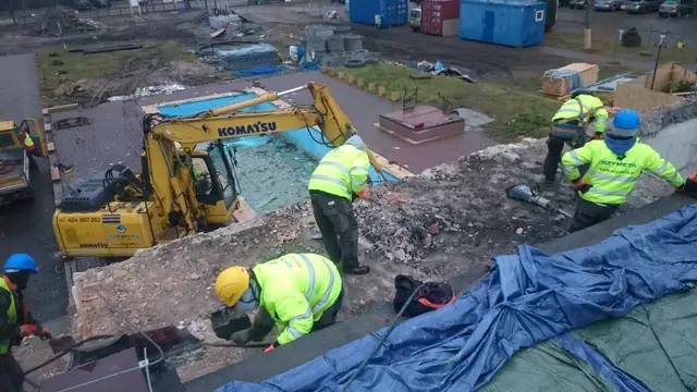Widok z góry na koparkę Komatsu rozbierającą fragment budynku obok kontenerów w Centrum Verano