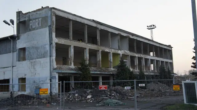 Budynek z napisem PORT ogrodzony siatką, gruz zalegający przy wejściu