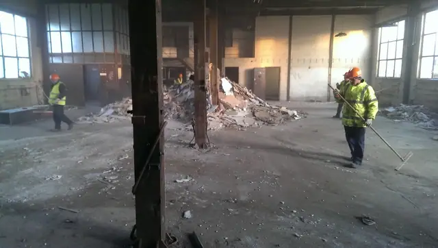 Pracownicy sprzątają gruz we wnętrzu hali po częściowej rozbiórce stropu