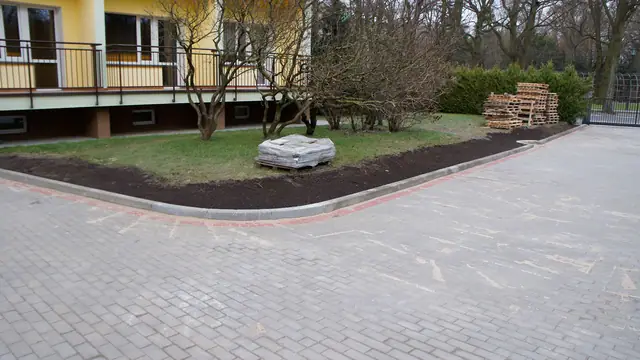 Narożnik placu z kostki brukowej obsadzony zielenią i głazem ozdobnym