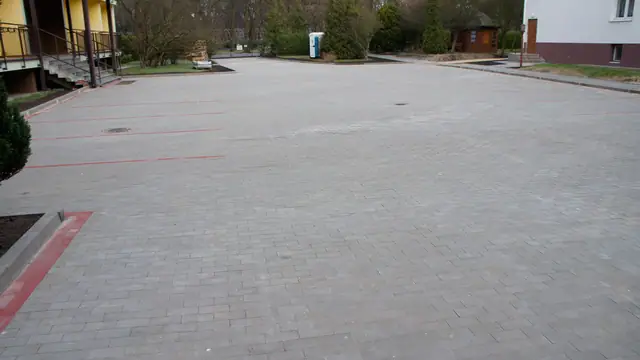 Obszerny parking z kostki brukowej z czerwonymi liniami wyznaczającymi miejsca postojowe