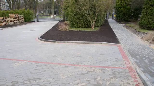 Wjazd na parking z kostki brukowej otoczony żywopłotem i metalową bramą