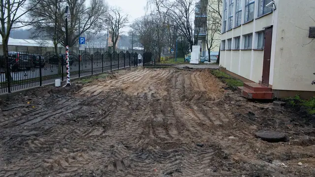 Wyrównany teren gruntowy wzdłuż metalowego ogrodzenia przy budynku sanatorium
