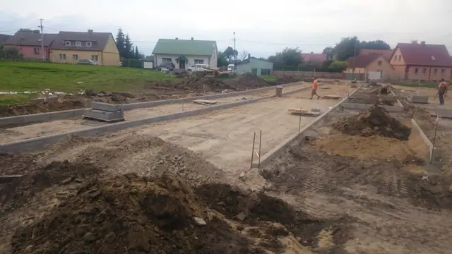 Szeroki widok formowanej alejki z krawężnikami i żwirową podbudową wzdłuż zabudowań