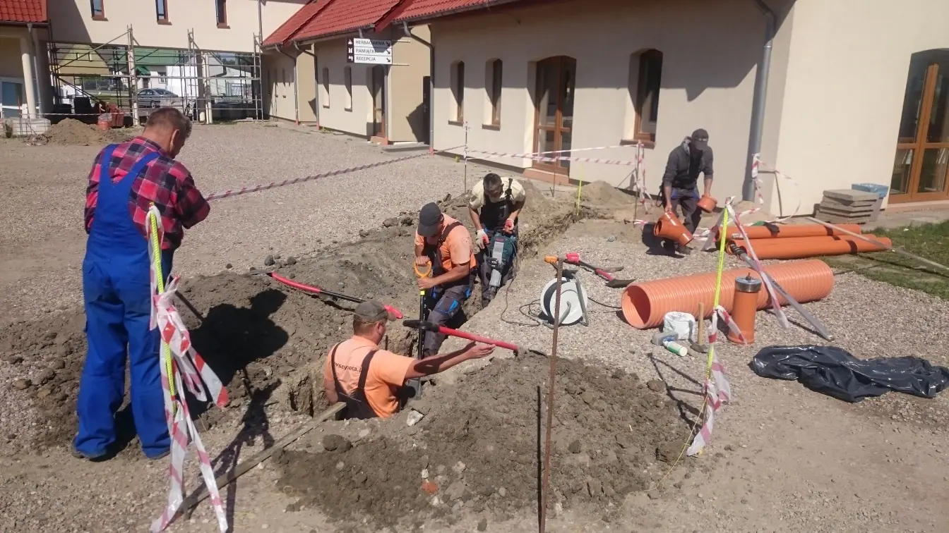 Montaż studzienki kanalizacyjnej z pomarańczowych rur przy elewacji budynku