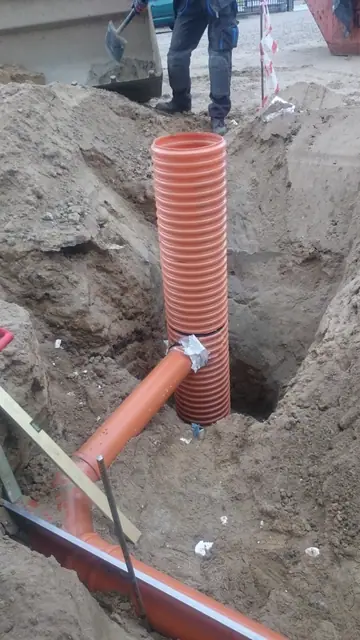 Pionowo osadzona studzienka z pomarańczowej rury karbowanej w głębokim wykopie ziemnym