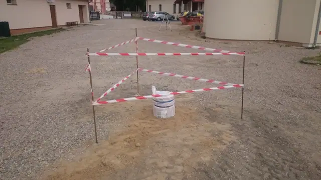 Taśma ostrzegawcza i wiadro oznaczają miejsce prac na żwirowym placu przy budynku