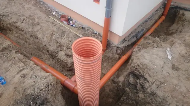 Zbliżenie na pionową rurę kanalizacyjną osadzoną przy narożniku fundamentu budynku