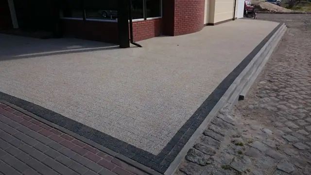 Wykończona nawierzchnia z płukanego betonu obramowana ciemnym krawężnikiem przy budynku