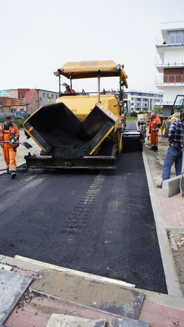 Finiszer z operatorem układa nawierzchnię asfaltową ścieżki przy krawężniku z czerwonej kostki