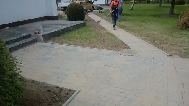 Robotnik zamiata gotowy chodnik z kostki brukowej na terenie ośrodka wypoczynkowego w Sianożętach