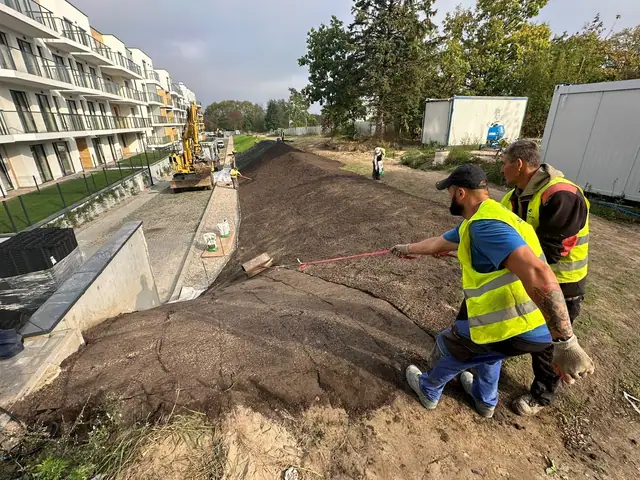 Robotnicy z taśmą mierniczą kontrolują nasyp ziemny obok bloków mieszkalnych w Ustroniu Morskim