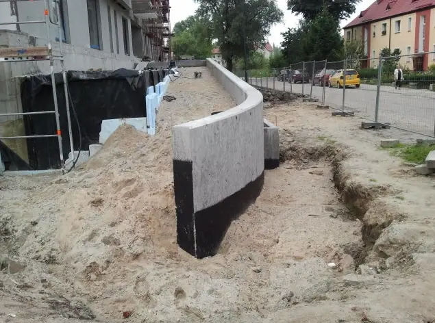 Łukowy mur oporowy z izolacją termiczną osadzony w piaszczystym wykopie przy budynku