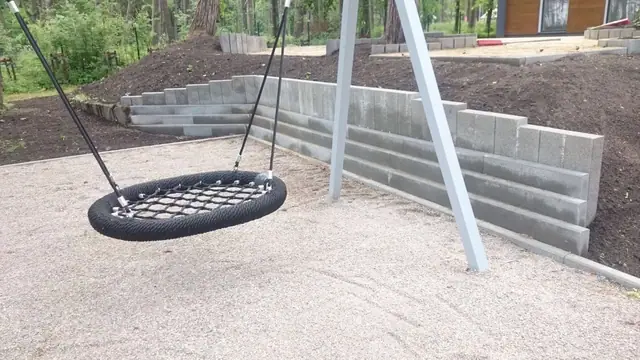 Huśtawka gniazdo na placu zabaw obok murku oporowego z betonowych schodków