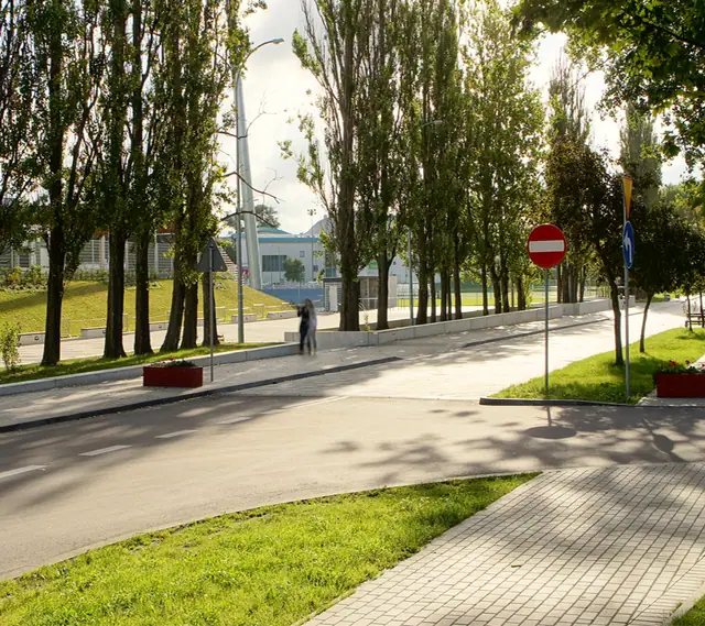 Ścieżka z kostki i chodnik z płyt wśród drzew na terenie kompleksu sportowego