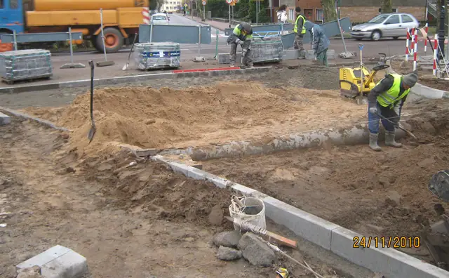 Wykop pod krawężnik z workami cementu, pracownik w kamizelce odblaskowej