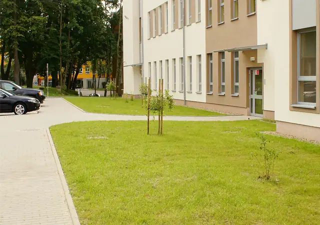 Chodnik z kostki brukowej prowadzący do wejścia budynku wśród nasadzeń trawnika przy Szpitalu w Koszalinie