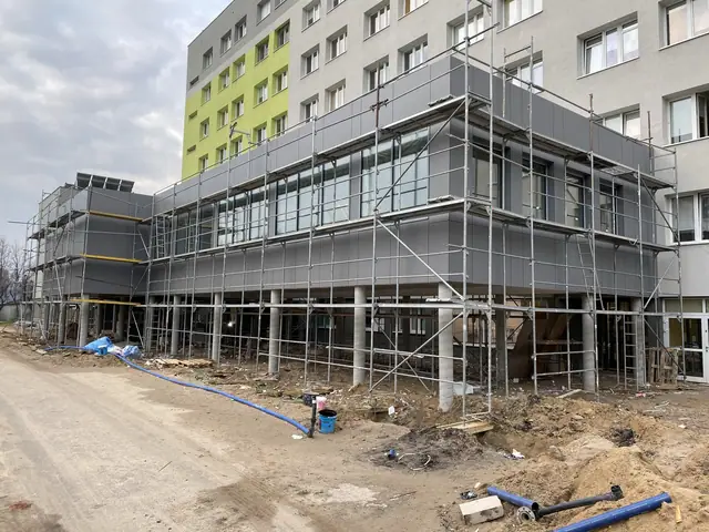 Inny kąt pawilonu szpitala w rusztowaniach z widoczną trwającą elewacją
