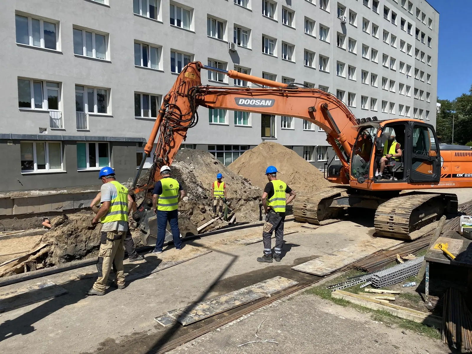 Koparka i ekipa pracują przy kopcu ziemi obok budynku szpitala podczas usług koparkowych w Kołobrzegu