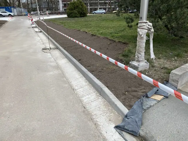 Świeżo osadzony krawężnik betonowy wzdłuż chodnika zabezpieczony taśmą ostrzegawczą