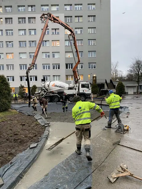 Pompa do betonu wylewa mieszankę na chodnik, pracownicy wygładzają powierzchnię