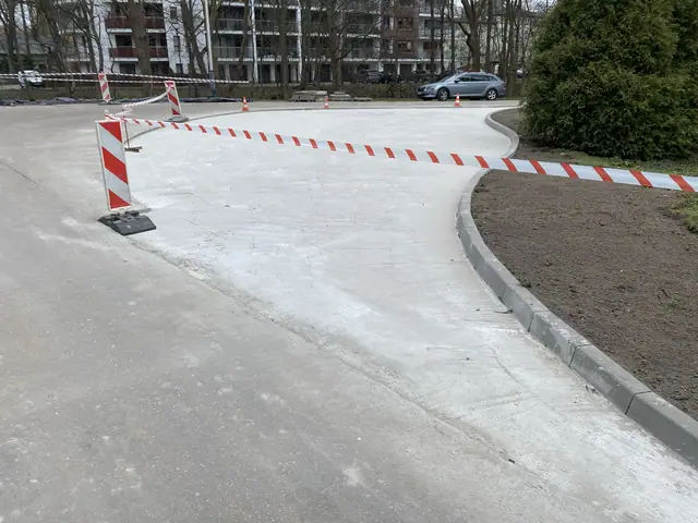 Zakrzywiony fragment nowej nawierzchni betonowej zabezpieczony pachołkami drogowymi