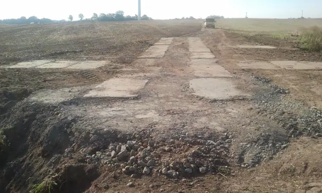 Droga z betonowych płyt technologicznych prowadząca przez pole, obsypana kamieniami po bokach