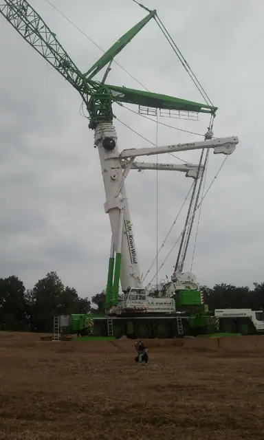 Rozłożony żuraw wieżowy podczas montażu elementów elektrowni wiatrowej na tle pochmurnego nieba