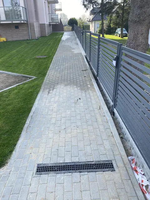 Długi chodnik z kostki brukowej wzdłuż ogrodzenia z metalowych szczebli