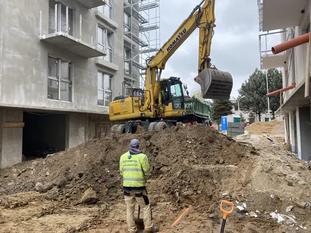 Koparka Komatsu wysypuje ziemię z łyżki przy wykopie z czerwonymi rurami