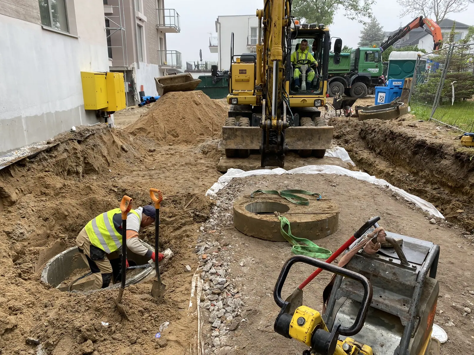 Koparka i zagęszczarka przy betonowych kręgach w głębokim wykopie – podobnie wygląda wykop pod szambo betonowe