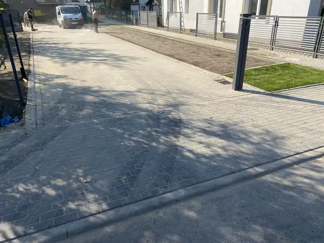 Świeżo utwardzony plac z kostki brukowej między budynkami, w tle koparka