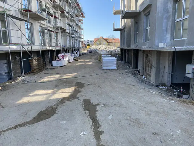 Utwardzony plac między budynkami z paletami materiałów budowlanych na osiedlu w Ustroniu Morskim