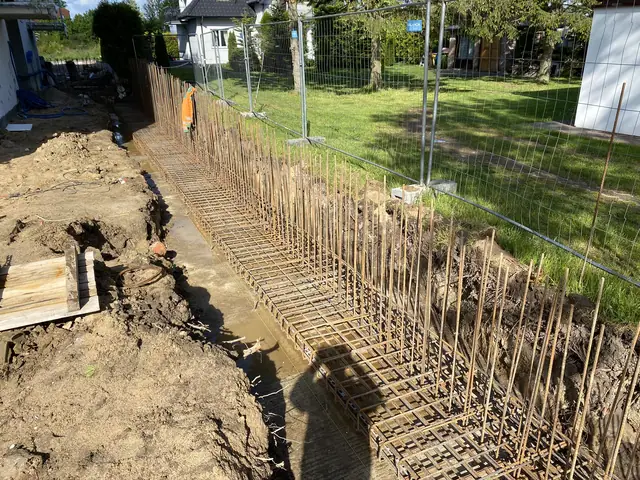 Zbrojenie muru oporowego ułożone wzdłuż ogrodzenia z siatki na trawniku