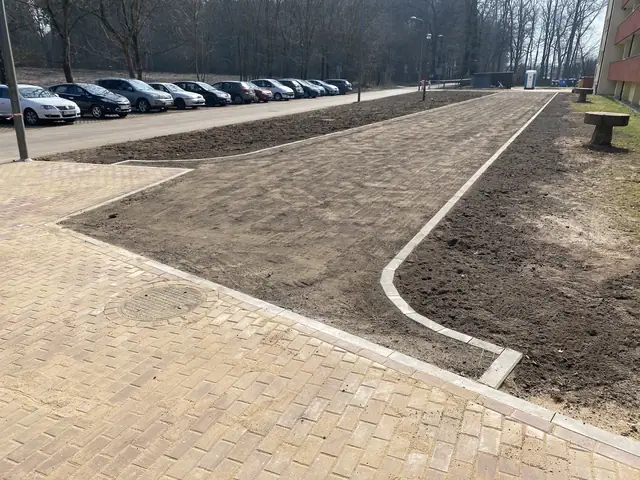 Aleja z kostki brukowej wzdłuż parkingu z trawnikiem po obu stronach