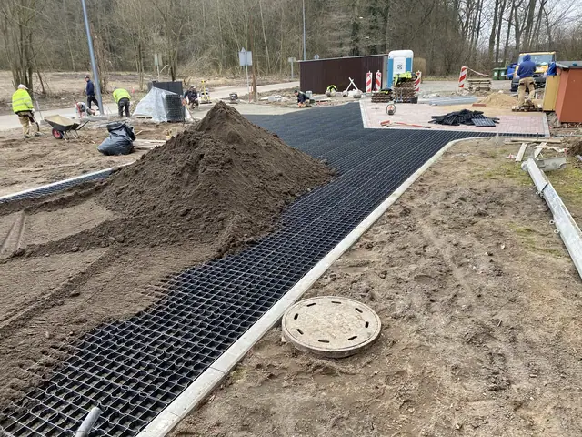 Robotnicy układają czarną kratę trawnikową na drodze pożarowej obok kopca ziemi