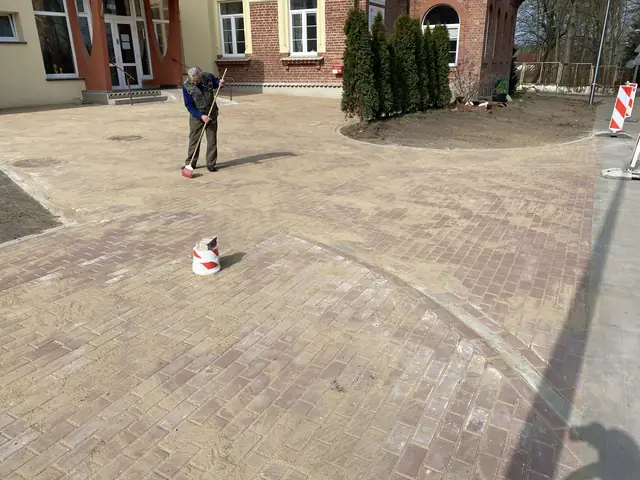 Robotnik grabi piasek fugujący na świeżo ułożonej kostce brukowej placu