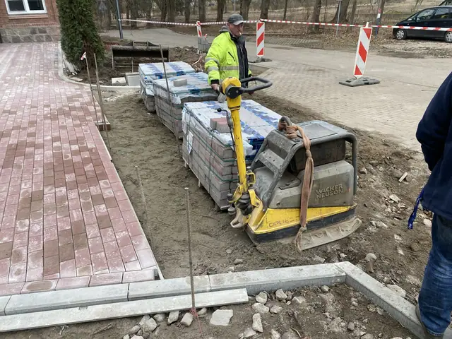 Robotnik prowadzi zagęszczarkę po paletach kostki brukowej przy chodniku z czerwonej kostki