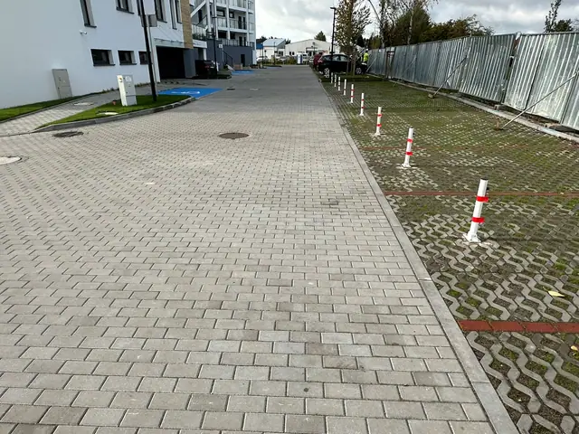 Droga z kostki brukowej wygrodzona taśmą i słupkami od strony sąsiedniej działki