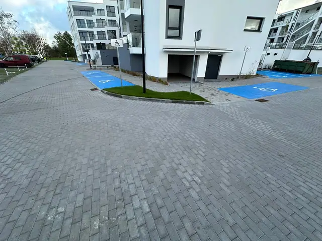 Parking z kostki brukowej z oznaczonymi miejscami dla niepełnosprawnych przy wejściu do budynku