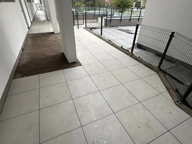 Ułożone jasne płyty chodnikowe na tarasie budynku mieszkalnego przy metalowym ogrodzeniu