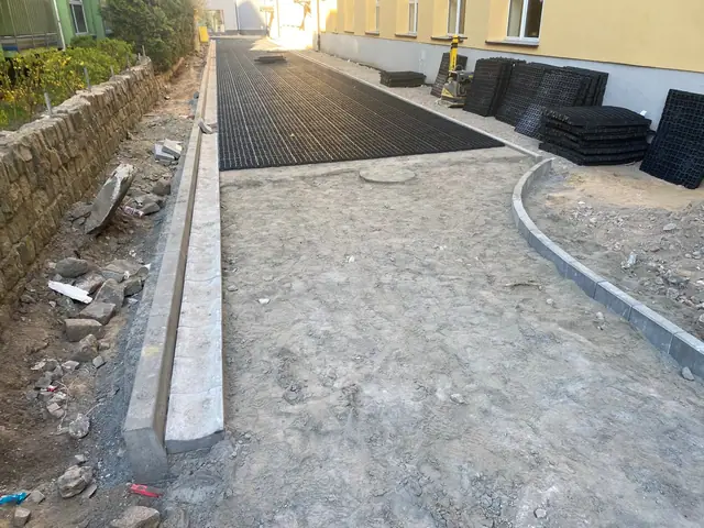 Ekipa układa czarną kratę trawnikową i zagęszcza podłoże na chodniku