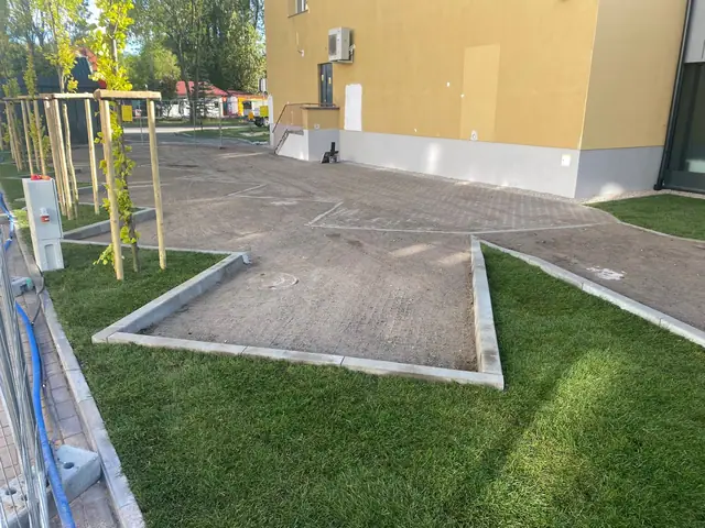 Geometryczny trawnik obramowany chodnikami z kostki przy budynku mieszkalnym