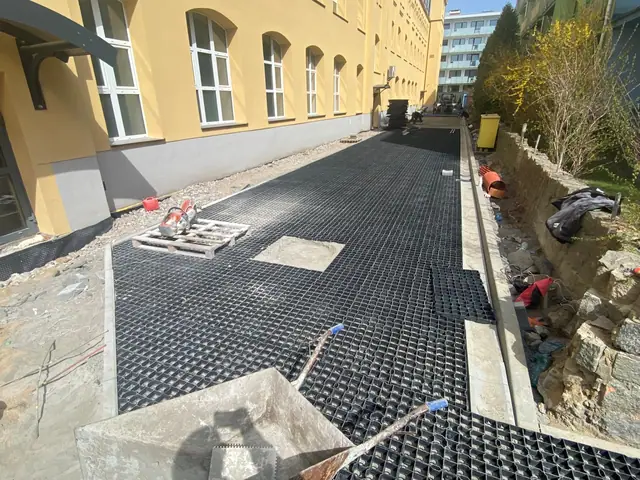 Czarna krata trawnikowa układana wzdłuż murku oporowego z kamieniami