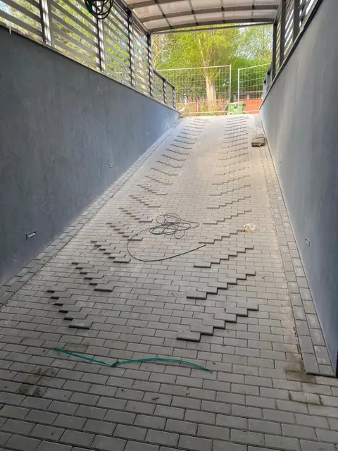 Pochylnia z kostki brukowej pod zadaszeniem przy zagospodarowanym terenie osiedla
