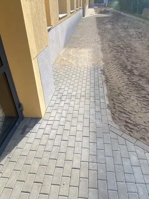 Ścieżka z kostki brukowej wzdłuż elewacji budynku z pasem piasku obok