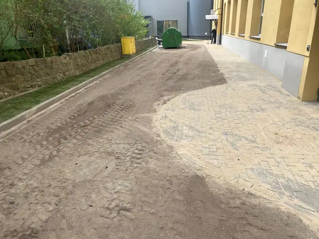 Ścieżka z kostki brukowej i piaszczysty pas gruntu przy wejściu do budynku