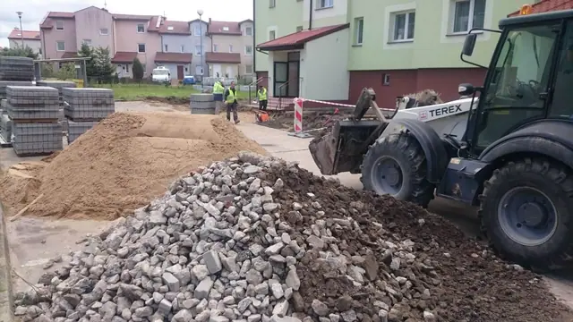 Koparka ładuje gruz rozbiórkowy na pryzmę obok pryzmy piasku na placu budowy