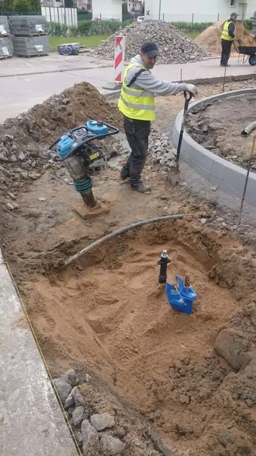 Pracownik montuje instalację w piaszczystym wykopie przy nowym obrzeżu chodnika