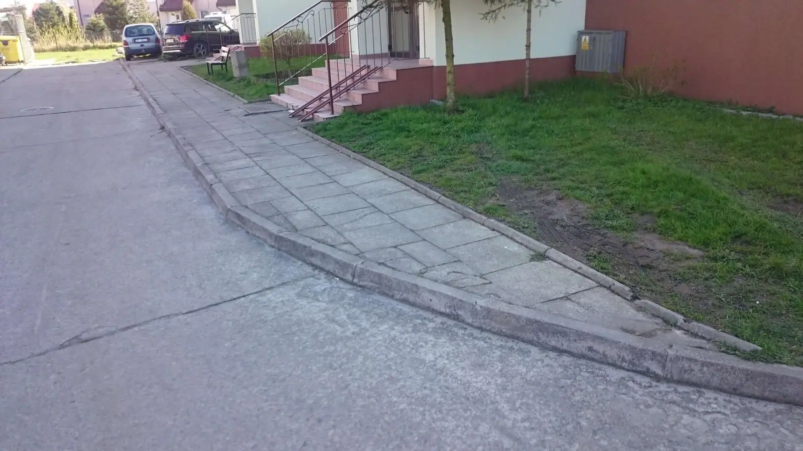 Stara popękana asfaltowa droga z krawężnikiem przed przebudową przy budynkach w Zieleniewie